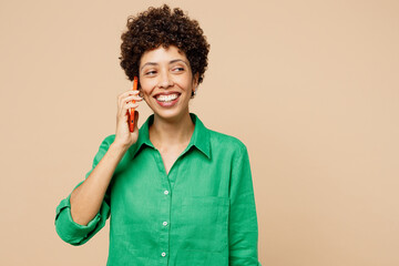 Young smiling cheerful woman of African American ethnicity wears green shirt casual clothes talk speak on mobile cell phone isolated on plain pastel light beige background studio. Lifestyle concept.