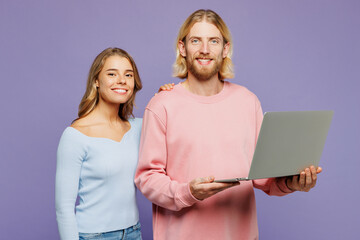 Young smiling happy couple two friends family IT man woman wear pink blue casual clothes together hold use work on laptop pc computer isolated on pastel plain light purple background studio portrait.