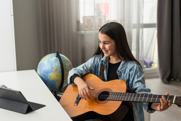 Teenager girl learning to play guitar at home using online lessons. Hobby remote musical education...