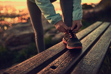 Person, hands and tying shoe with hiker on bench for morning walk or trekking on outdoor mountain....