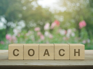 Coach letter on wood block cubes on wooden table over blur pink flower and tree in garden,...
