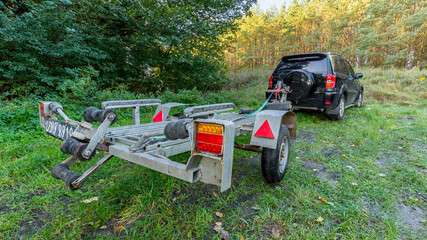 black off-road vehicle, boat transport trailer, parked on green grass, by the lake, fishing...