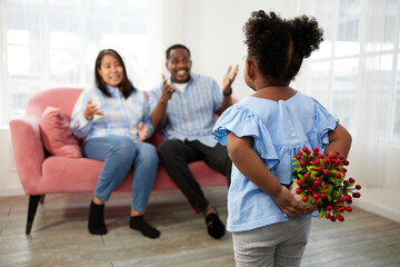 African child girl hiding red flowers for surprise her father and mother behind her back in the home