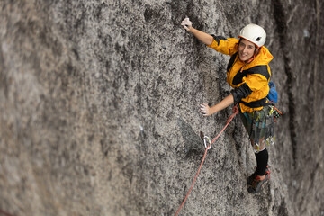 A woman is climbing a rock wall wearing a yellow jacket and a helmet