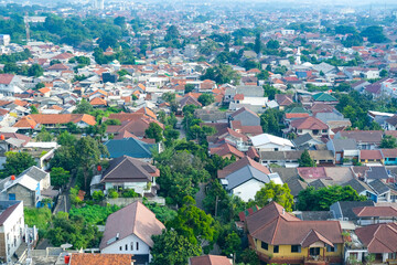 Obraz premium A panoramic view of Bogor city with densely packed houses, green trees, and distant mountains covered in light mist, showcasing the balance of urban life and natural beauty
