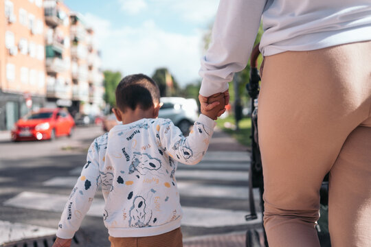 Mother and child walking hand in hand on city street. Close-up of a mother holding her child's hand while walking on an urban zebra crossing