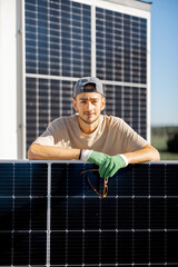Portrait of a man standing with solar panel on a rooftop of his house during installation process. Owner of property installing solar panels for self consumption