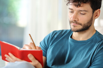 Serious man writing on agenda at home