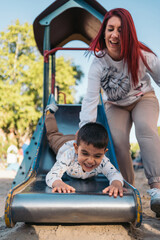 Joyful playtime at the park with mom. Laughing autistic boy slides down as his mother cheers him on at a sunny playground