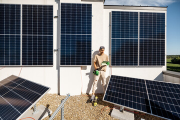 Technician with a digital tablet checks the operation of a newly installed solar station on the roof of a house. The concept of maintenance of solar plants and their performance