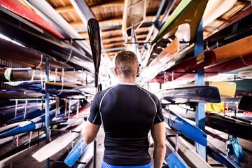 Portrat of young canoeist standing in the middle of stacked canoes. Concept of canoeing as dynamic...