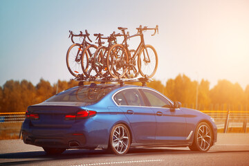 Blue sedan car traveling on highway with four bicycles mounted on a roof rack against a clear blue...