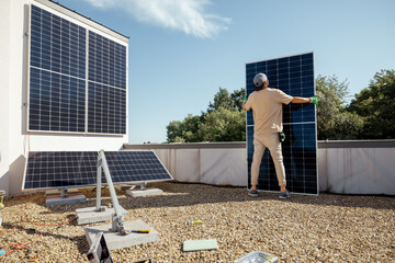 Man carries solar panel while installing solar plant of a rooftop of his property. Wide angle view....