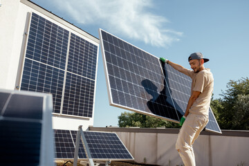 Man carries solar panel while installing solar plant of a rooftop of his property. Wide angle view. Renewable energy for self consumption concept. Idea of installing panels for households