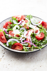 Salad with fresh tomatoes and arugula on a bright stone background. Close up. Copy space.