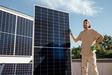 Portrait of a man standing with solar panel on a rooftop of his house during installation process....