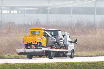 Roadside assistance. Tow truck transporting a broken car on a highway. Flatbed towing truck with a...