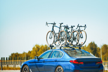 Blue sedan car traveling on highway with four bicycles mounted on a roof rack against a clear blue...