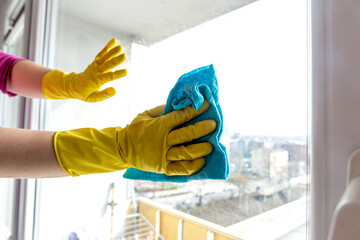 Female hand in yellow gloves washes the window with blue rag