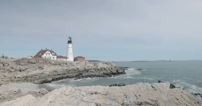Beautiful rocky sea side view of the Portland Maine Head Light light house during a beautiful spring day with waves rolling into the rocky shore in 4k.