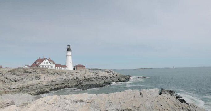 Beautiful rocky sea side view of the Portland Maine Head Light light house during a beautiful spring day with waves rolling into the rocky shore in 4k.