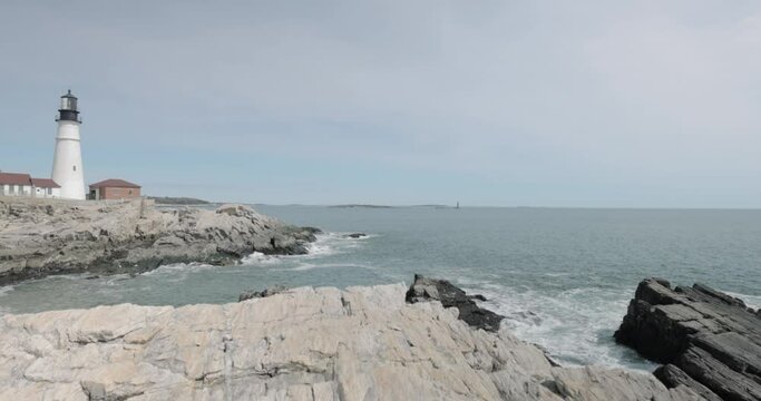 Beautiful rocky sea side view of the Portland Maine Head Light light house during a beautiful spring day with waves rolling into the rocky shore in 4k.