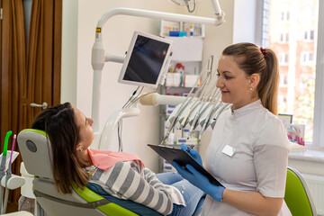 Female dentist explaining about oral care treatment service with tablet to caucasian woman patient