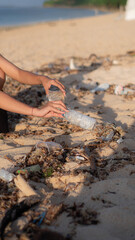 A woman's hand is seen collecting a plastic bottle from the beach, symbolizing the spirit of volunteerism.
