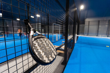 Black professional paddle tennis racket and ball with natural lighting on blue background....