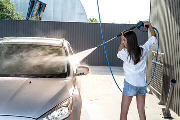 Pretty slim woman cleaning her car using high pressure water gun.