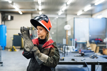 Beautiful blonde woman works as a welder in workshop, operating welding machine, wearing protective...