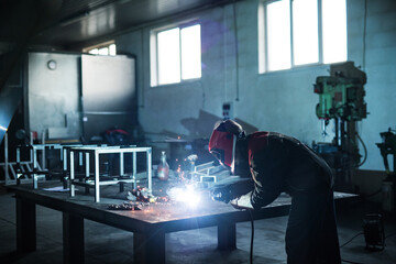 Beautiful blonde woman works as a welder in workshop, operating welding machine, wearing protective...