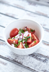 Simple salad with cherry tomatoes, red onion and fresh herbs. Bright wooden background. Copy space.