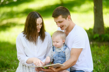  Happy family with toddler enjoying their holiday together, relaxing during picnic in park, reading...