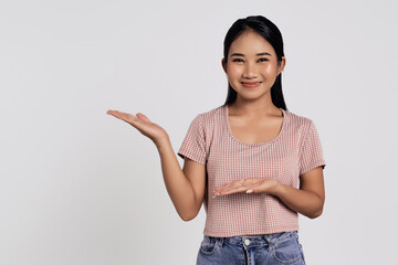 Smiling happy young Asian woman wearing casual clothes pointing her hands arms aside on area...
