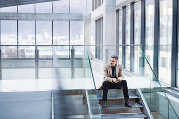 Handsome businessman sitting on stairs in modern office hallway.
