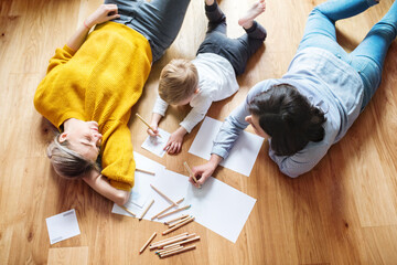 Three generations. Mother, grandmother and little boy drawing, lying on floor, holding crayons.