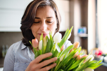 Portrait of beautiful mature woman with black hair and soft smile, holding bouquet of tulips.