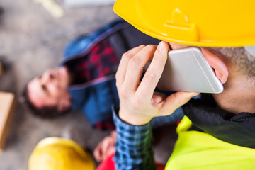 Colleague giving first aid to unconscious worker after accident, calling ambulance. Concept of...