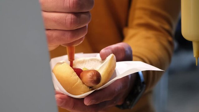 Adding ketchup and mayonnaise on Hot Dog. American Fast Food. Tasty unhealthy meal. Street food. Grilled Sausage on white bread bun. Public catering self-service in airport, shop, railway bus station