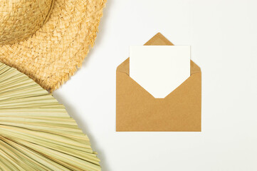 Top view of straw hat, dried palm leaf on white background. Brown kraft envelope, white card, post....