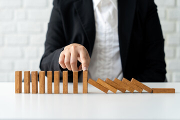 Businesswoman's hands trying to stop falling dominoes on table.