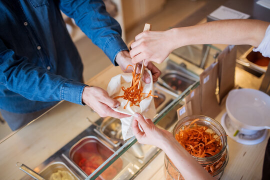 Handsome shop assistant serving customer in package-free store using reusable containers. Zero waste shops offering package-free bulk goods and sustainable alternatives.