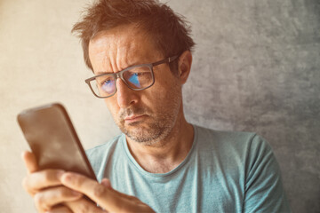 Portrait of casual authentic mature adult male with eyeglasses using smartphone indoors