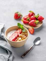 Natural greek yogurt with granola and strawberries in a bowl on a blue background with fresh berries and spoon.
