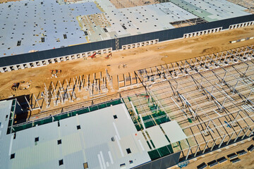 Aerial view of construction site with warehouse building under construction for storage. Assembling industrial building with steel frame structure and roof truss. Infrastructure for logistics