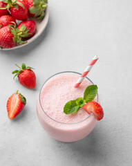 A glass of fresh strawberry smoothie with mint on a light background with fresh berries.