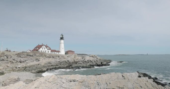 Beautiful rocky sea side view of the Portland Maine Head Light light house during a beautiful spring day with waves rolling into the rocky shore in 4k.