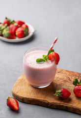 A glass of fresh strawberry smoothie with mint on a wooden board on a light background with fresh berries.