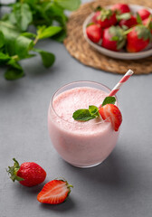A glass of fresh strawberry smoothie on a blue background with fresh berries and mint.